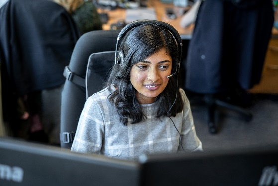 Foto einer Frau, die ein Headset trägt und vor Computermonitoren sitzt.