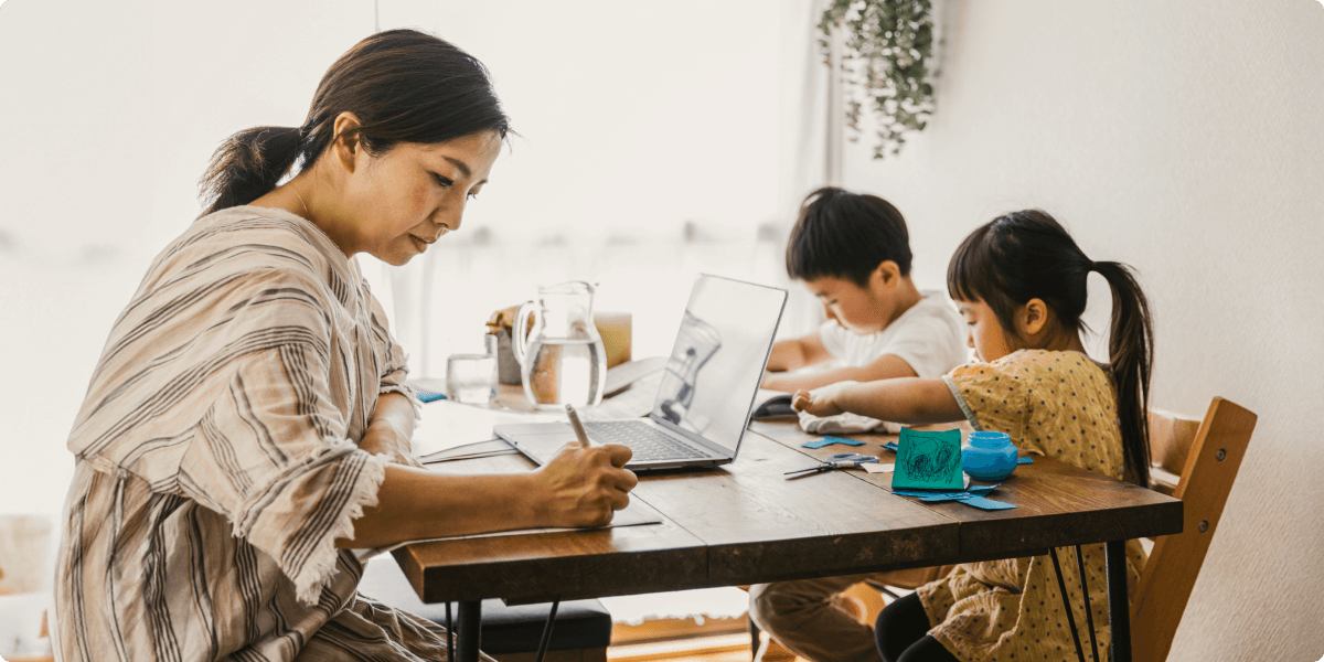 Eine Frau, die am Tisch des Esszimmers arbeitet, mit ihren Kindern, die basteln.