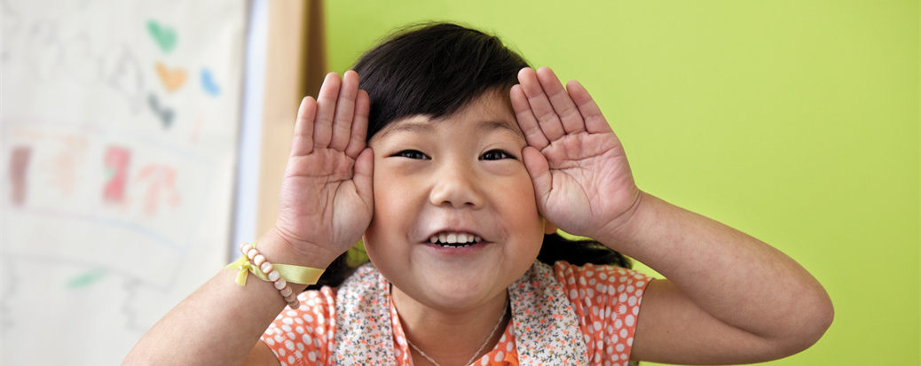 Photo of a young girl holding her hands up to her ears to indicate she is listening to the viewer's words.