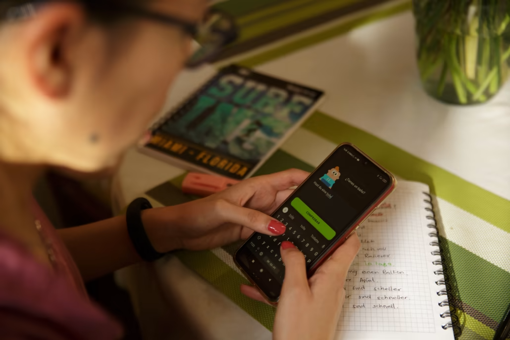 Screenshot of a person at a desk on a mobile phone using the Duo Lingo app.