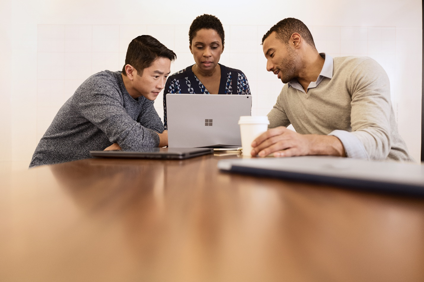 A photograph showing 3 people in meeting, looking at a laptop.