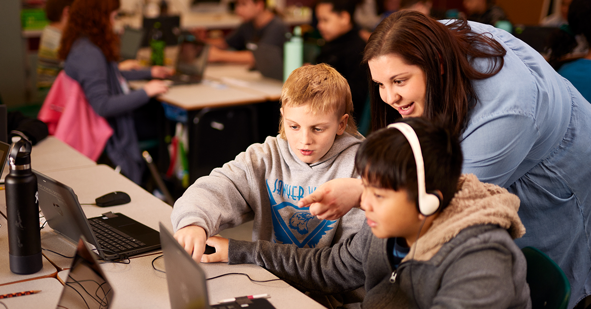 Photo of a teacher assisting two young students engaged in game-based learning.