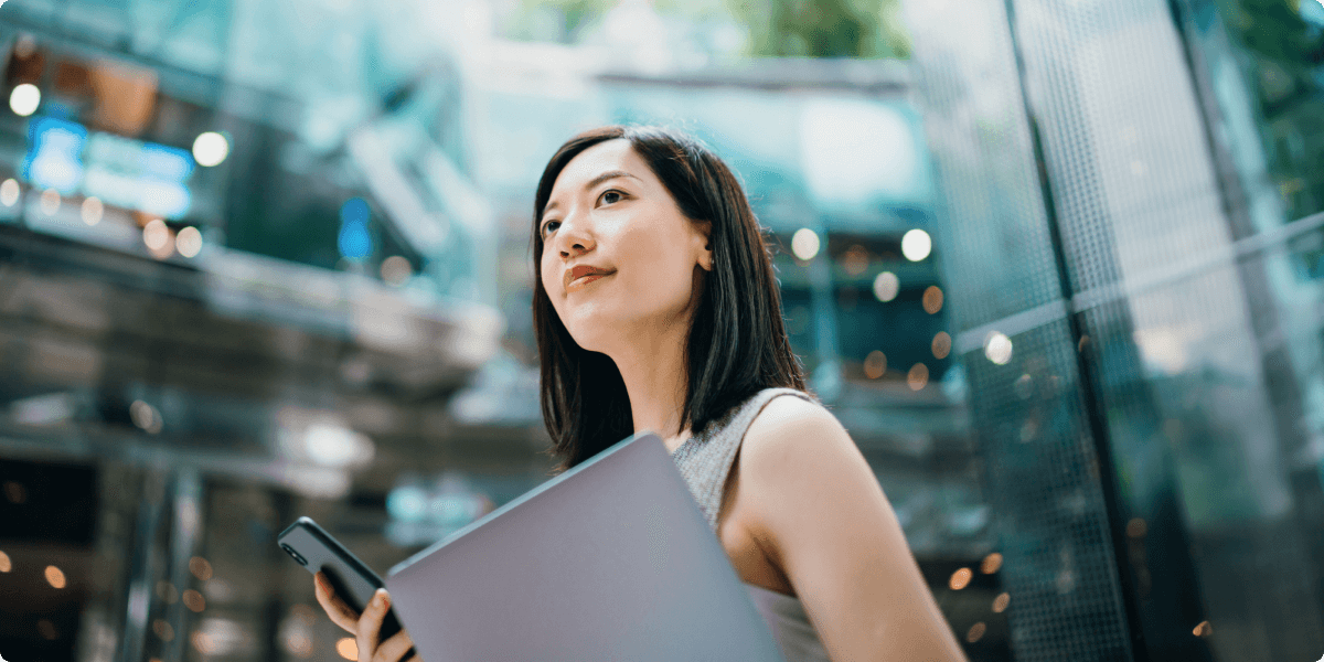 A woman holding a laptop and cellphone, looking uplifted and capable.