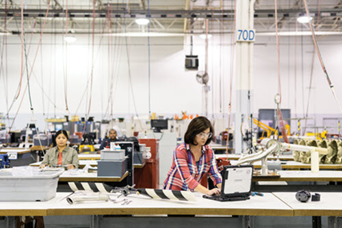 Photograph showing woman in manufacturing working at a table on a computer.