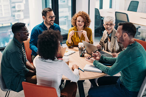 Photograph showing people working and talking around a table.