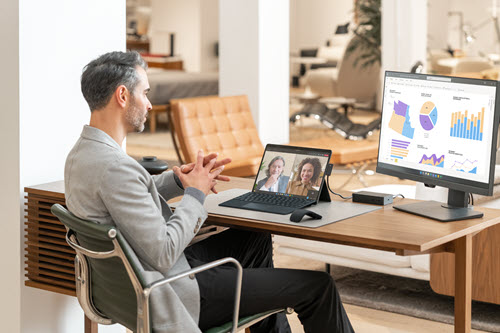 Photograph showing person at a desk in a video call while reviewing reports.