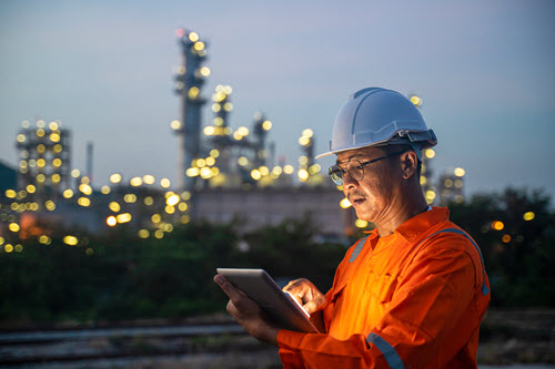 Photograph showing of a worker in a hard hat looking at a tablet  while working on solar panels.