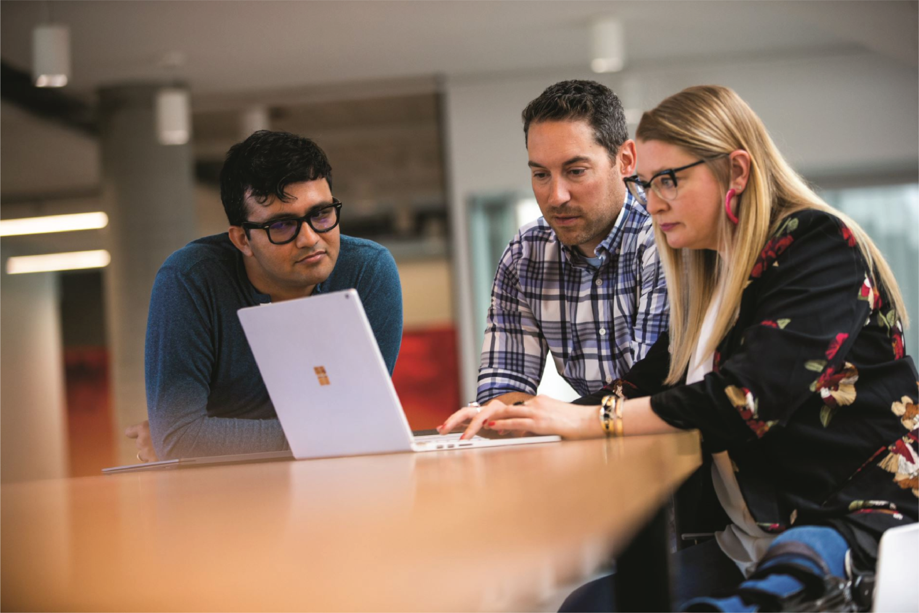 Kolme ihmistä istuu yhdessä pöydän ääressä Microsoft Surface -kannettavan edessä.