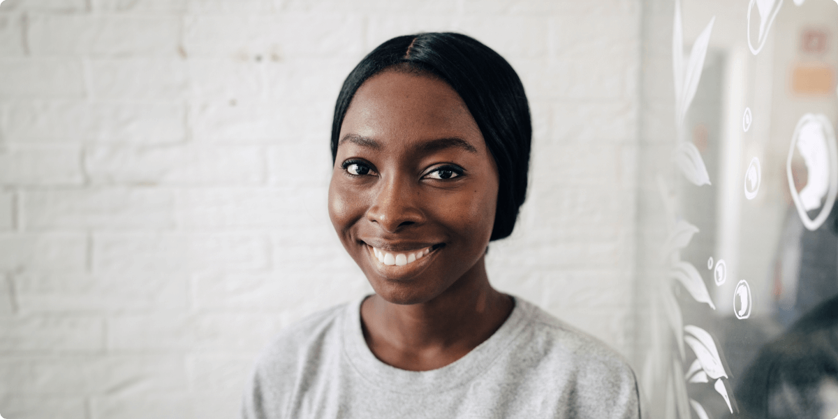 Portrait d’une femme souriante devant un mur en briques blanc.