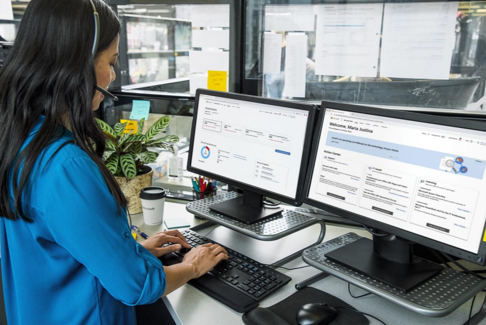 Donna in piedi alla scrivania di un ufficio con due monitor uno accanto all'altro.