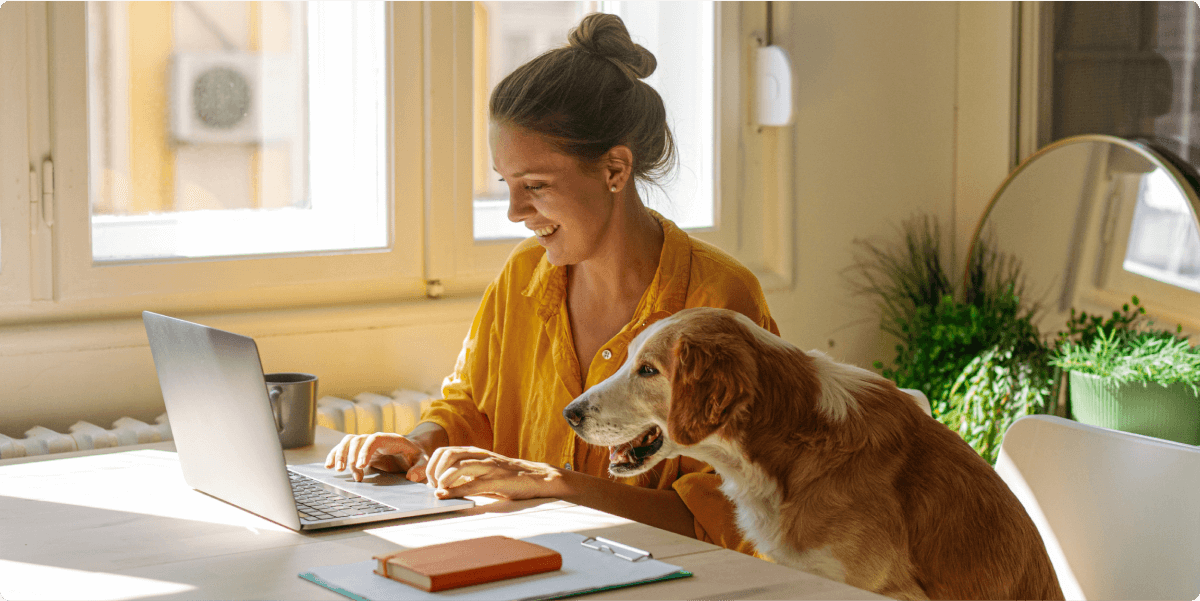 Een vrouw die op haar laptop werkt met haar hond in de buurt.