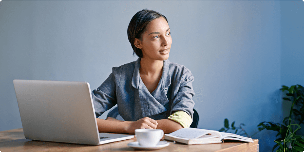 Een vrouw die in een thuiskantoor werkt met notitieblokken, laptop en theecup.