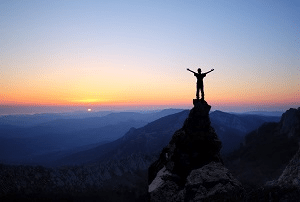 Uma pessoa que está em uma montanha ao pôr do sol