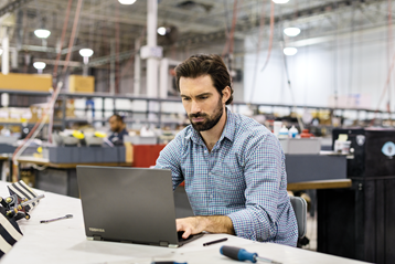 Imagem de um empresário genérico usando um computador em uma configuração de fabricação.