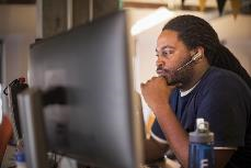 Foto de um homem usando um fone de ouvido e sentado em um computador.