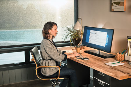 Foto de uma mulher trabalhando em um computador sentada em uma mesa.