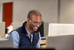 Um homem sorrindo para um monitor de computador.