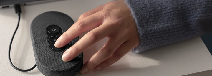 An image of a hand pressing a USB speaking device with large buttons on it for volume and muting.